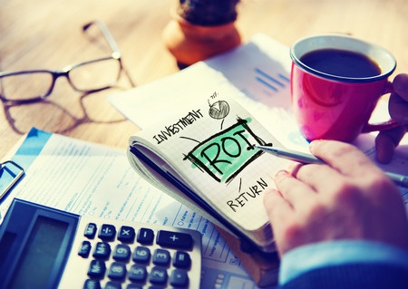 Closeup photo of person's hand with coffee and notepad that says "ROI" for return on investnement